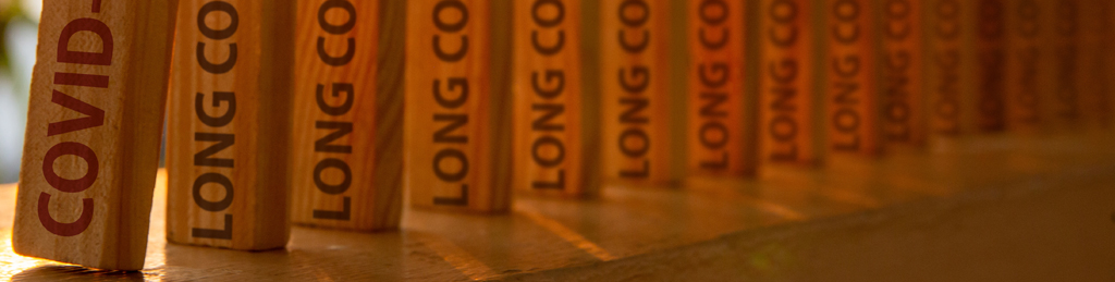 Holzsteine mit der Aufschrift „Long Covid“ in einer Reihe, die umzufallen drohen (Domino-Effekt)
